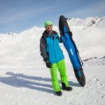 Mann mit Skitasche auf der Piste