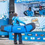 Mann mit Snowboardbag vor Buehne mit DJ